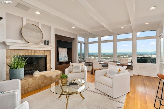 living room with a tiled fireplace, hardwood / wood-style floors, beamed ceiling, and ornamental molding