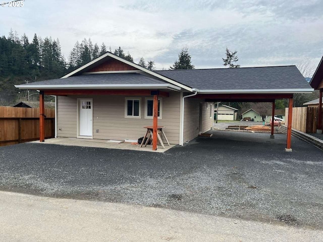 view of front facade featuring an attached carport, a shingled roof, fence, and gravel driveway