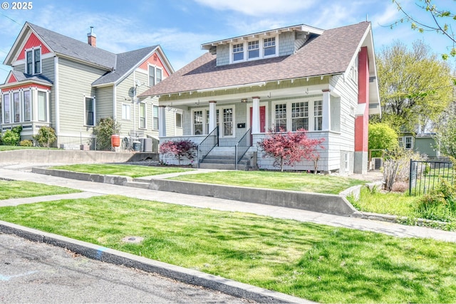 view of front of home featuring a front lawn, fence, a shingled roof, and covered porch