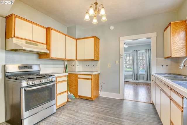 kitchen with a chandelier, gas range, under cabinet range hood, a sink, and decorative backsplash