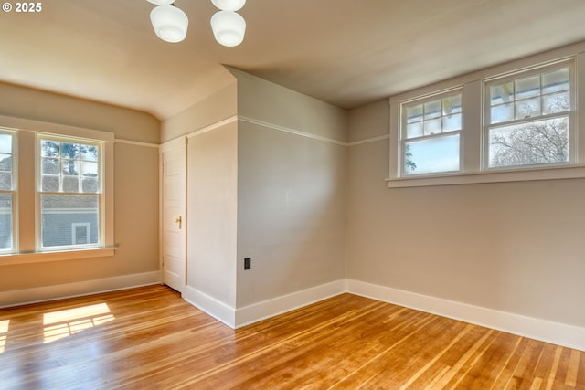 empty room with light wood-style flooring, a notable chandelier, and baseboards