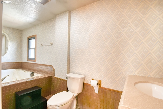 full bathroom with toilet, a textured ceiling, vanity, a jetted tub, and wallpapered walls