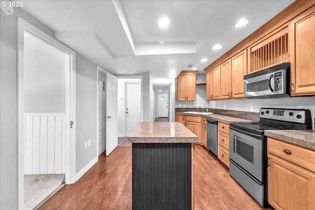 kitchen with a kitchen island, appliances with stainless steel finishes, a sink, and light wood-type flooring