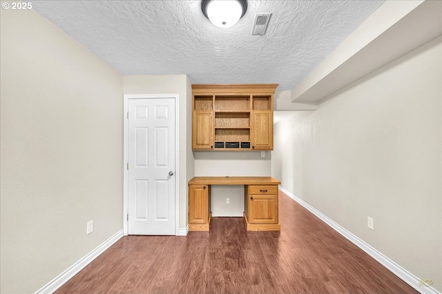 unfurnished office with baseboards, dark wood-style flooring, a textured ceiling, and visible vents