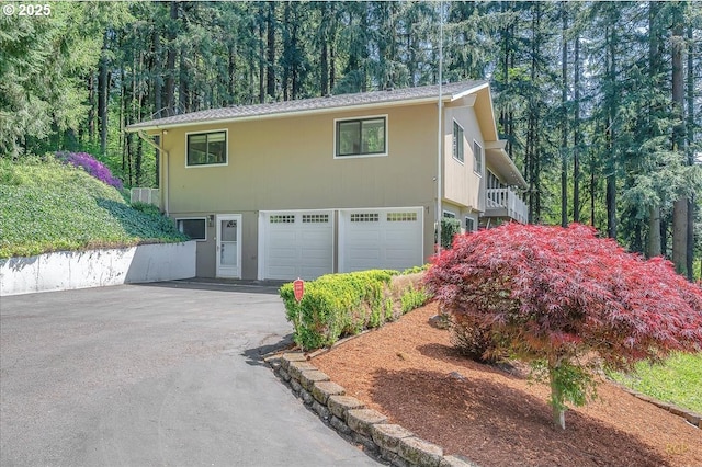 view of side of home featuring a garage, aphalt driveway, and a wooded view