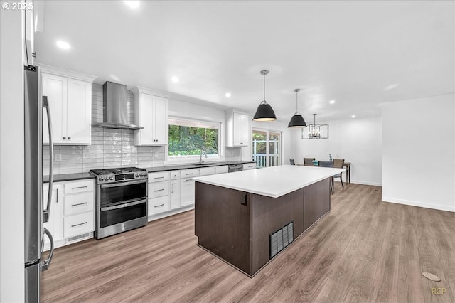 kitchen featuring a sink, light wood finished floors, wall chimney exhaust hood, stainless steel appliances, and decorative backsplash