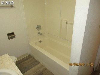 646/648 W Sixth Ave, Sutherlin, OR 97479 - full bath featuring wood finished floors, toilet, shower / bathtub combination, vanity, and baseboards