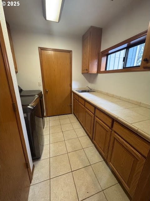 kitchen with light tile patterned flooring, sink, washer and clothes dryer, and tile counters