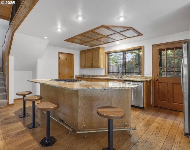 bar with light hardwood / wood-style flooring, light stone counters, a kitchen island, stainless steel appliances, and a breakfast bar area