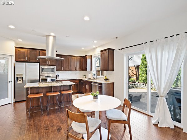 15582 SE Owl Ln, Happy Valley, OR 97015 - kitchen with appliances with stainless steel finishes, island exhaust hood, dark brown cabinets, a kitchen island, and recessed lighting