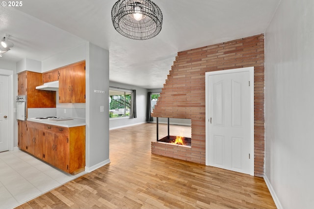 2431 W Crestview Ave, Roseburg, OR 97471 - kitchen featuring white appliances, under cabinet range hood, light wood finished floors, a brick fireplace, and light countertops
