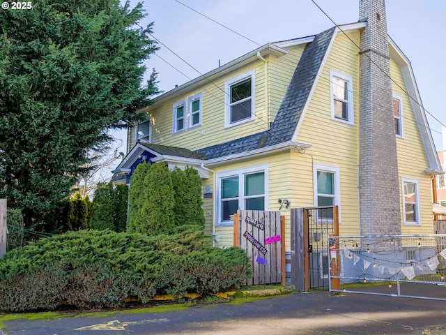 view of front of home featuring a shingled roof, fence, a gambrel roof, a chimney, and a gate