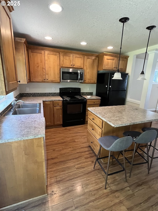 6721 N Yale St, Portland, OR 97203 - kitchen with black appliances, wood finished floors, a kitchen bar, a textured ceiling, and recessed lighting