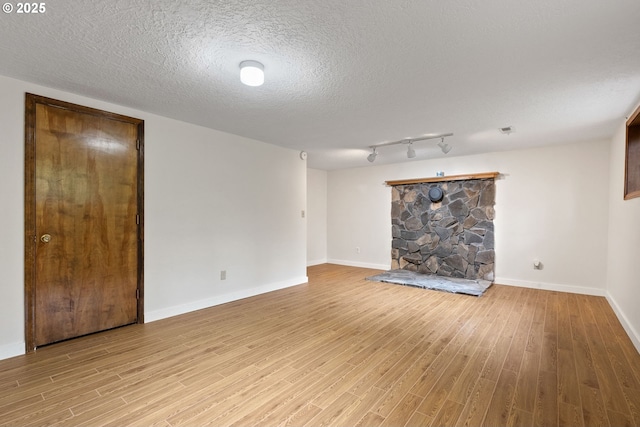 unfurnished room featuring light wood-type flooring, baseboards, a stone fireplace, and a textured ceiling