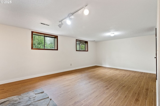 unfurnished room featuring a textured ceiling, wood finished floors, baseboards, and rail lighting