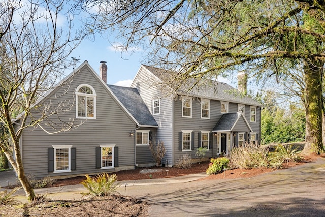 colonial inspired home with a chimney and a shingled roof