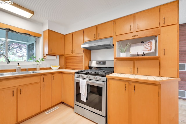 2801 Kincaid St, Eugene, OR 97405 - kitchen featuring stainless steel gas stove, under cabinet range hood, a sink, light wood-type flooring, and tile counters