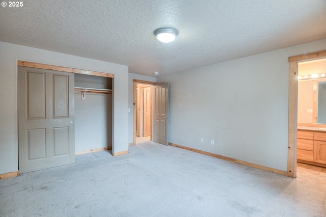 unfurnished bedroom with connected bathroom, light colored carpet, a textured ceiling, and a closet