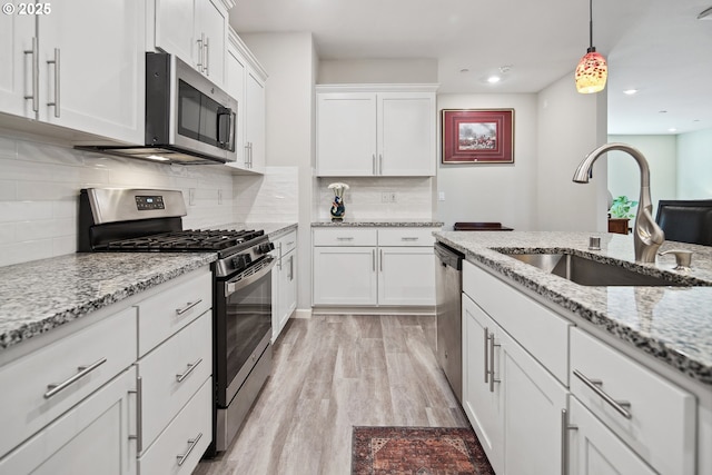 kitchen featuring light wood finished floors, decorative light fixtures, appliances with stainless steel finishes, white cabinetry, and a sink