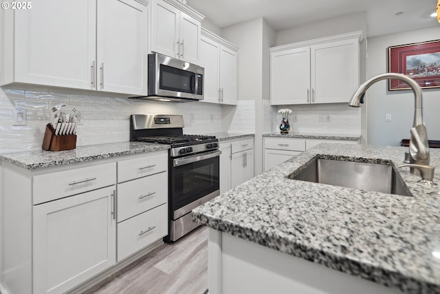 kitchen featuring light wood finished floors, a sink, decorative backsplash, stainless steel appliances, and white cabinetry