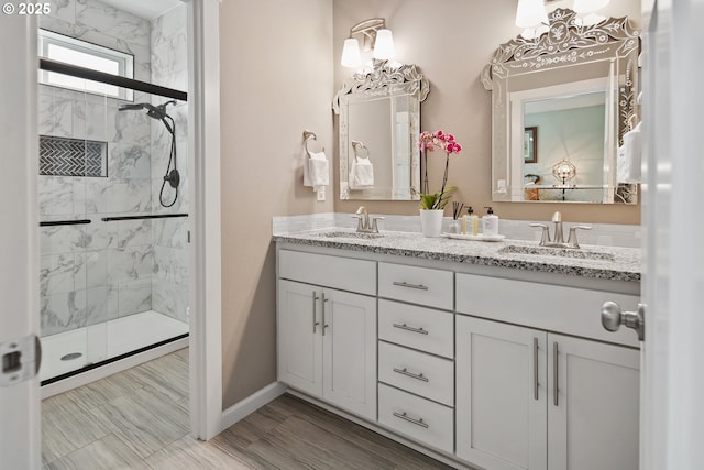 full bathroom featuring a sink, a marble finish shower, baseboards, and double vanity