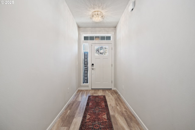 entryway with baseboards, an inviting chandelier, and light wood finished floors