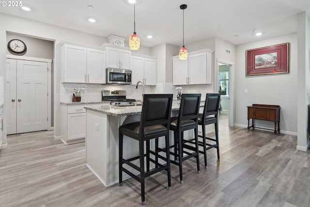 kitchen featuring stainless steel appliances, light wood-style floors, white cabinetry, a kitchen breakfast bar, and tasteful backsplash