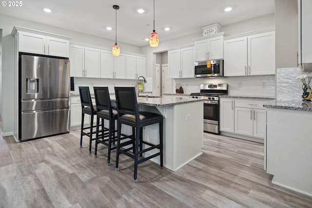 kitchen with stainless steel appliances, light wood finished floors, a kitchen breakfast bar, and white cabinetry