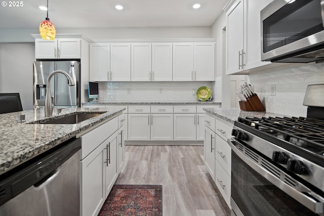 kitchen featuring light wood finished floors, tasteful backsplash, appliances with stainless steel finishes, white cabinetry, and a sink