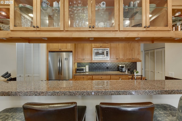 844 SW Broadway Dr Unit 3, Portland, OR 97201 - kitchen with appliances with stainless steel finishes, decorative backsplash, a breakfast bar area, tile counters, and glass insert cabinets