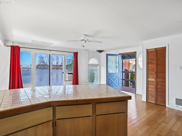 kitchen with visible vents, a water view, tile countertops, light wood finished floors, and ceiling fan