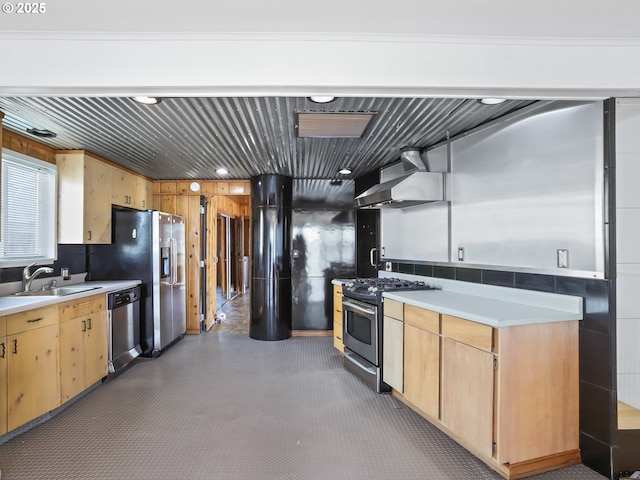 kitchen featuring a sink, appliances with stainless steel finishes, light countertops, and wall chimney range hood