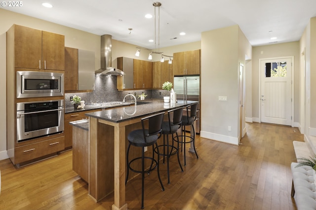 10122 SW Morrison St, Portland, OR 97225 - kitchen featuring stainless steel appliances, wall chimney range hood, brown cabinets, a breakfast bar area, and decorative backsplash