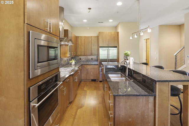 10122 SW Morrison St, Portland, OR 97225 - kitchen featuring stainless steel appliances, wall chimney exhaust hood, a kitchen breakfast bar, a center island with sink, and brown cabinets