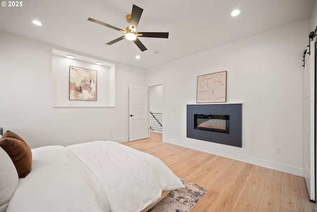 118 W 13th Way, La Center, WA 98629 - bedroom featuring a barn door, light wood-type flooring, recessed lighting, baseboards, and a glass covered fireplace