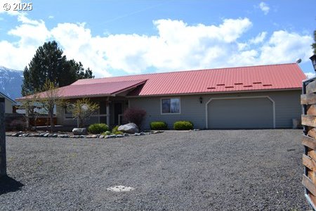 ranch-style house featuring an attached garage, driveway, and metal roof