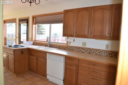 kitchen with tile countertops, white dishwasher, light tile patterned floors, cooktop, and a sink