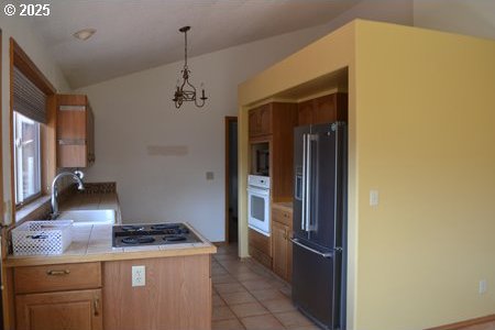 kitchen featuring white oven, high quality fridge, a sink, lofted ceiling, and an inviting chandelier