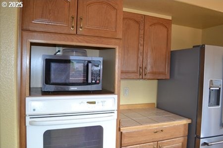 kitchen featuring tile countertops, appliances with stainless steel finishes, and brown cabinetry