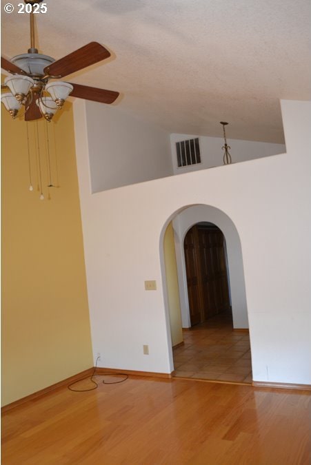 spare room featuring visible vents, a ceiling fan, light wood-style floors, arched walkways, and vaulted ceiling