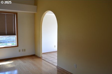 empty room featuring baseboards, arched walkways, and wood finished floors