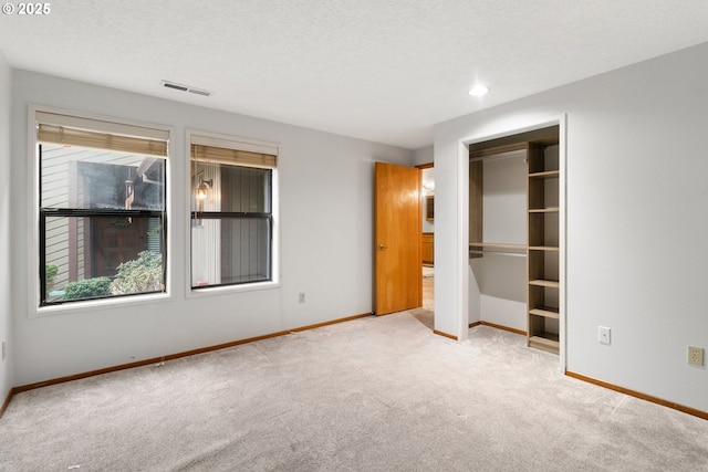 unfurnished bedroom with a textured ceiling, multiple windows, carpet, and baseboards