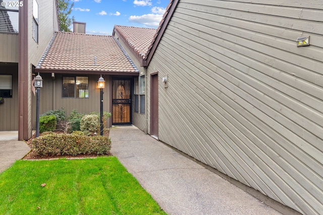 view of exterior entry featuring a lawn and a tiled roof