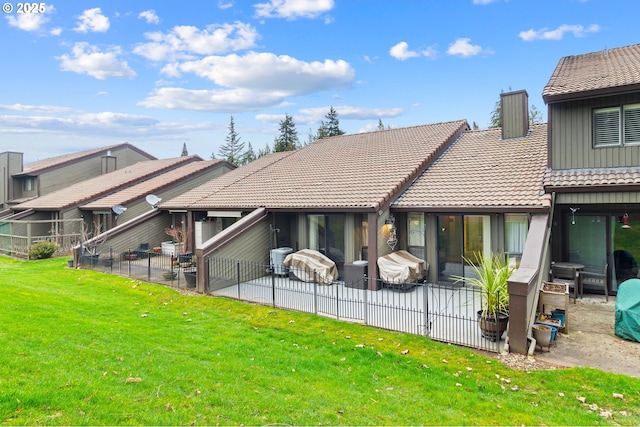 rear view of house featuring a yard, a tile roof, a patio, and fence