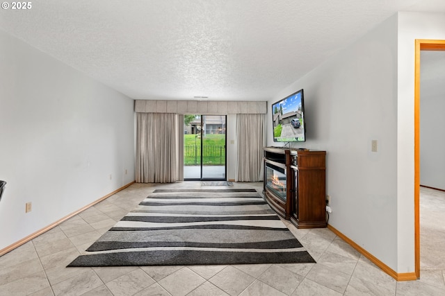 living area featuring a glass covered fireplace, a textured ceiling, and baseboards