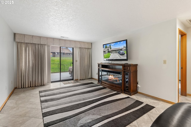 tiled living area with a glass covered fireplace, visible vents, a textured ceiling, and baseboards