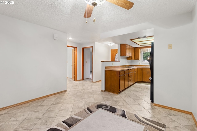 kitchen featuring baseboards, brown cabinetry, a ceiling fan, a peninsula, and light countertops