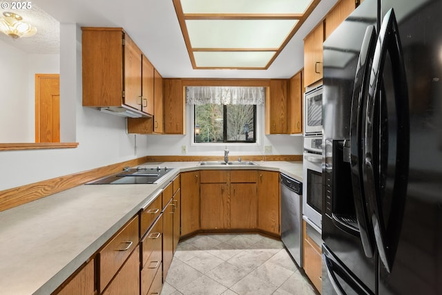 kitchen featuring brown cabinets, light countertops, light tile patterned flooring, a sink, and black appliances