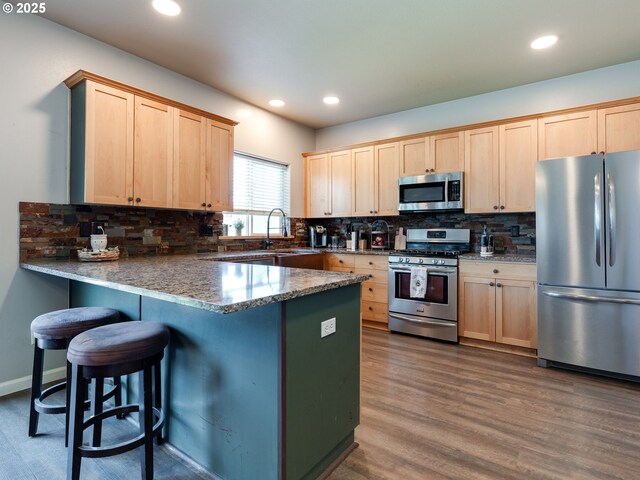 kitchen featuring appliances with stainless steel finishes, light brown cabinetry, a peninsula, tasteful backsplash, and recessed lighting