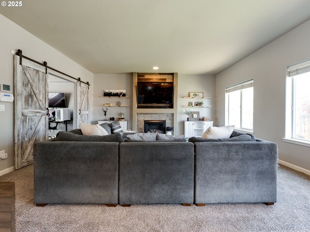 carpeted living room with a barn door, baseboards, and a fireplace